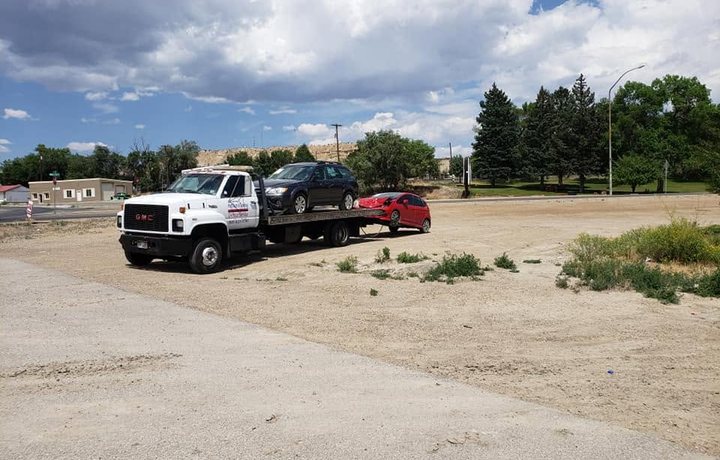 GMC flatbed carrying a station wagon with a small red car towed behind it